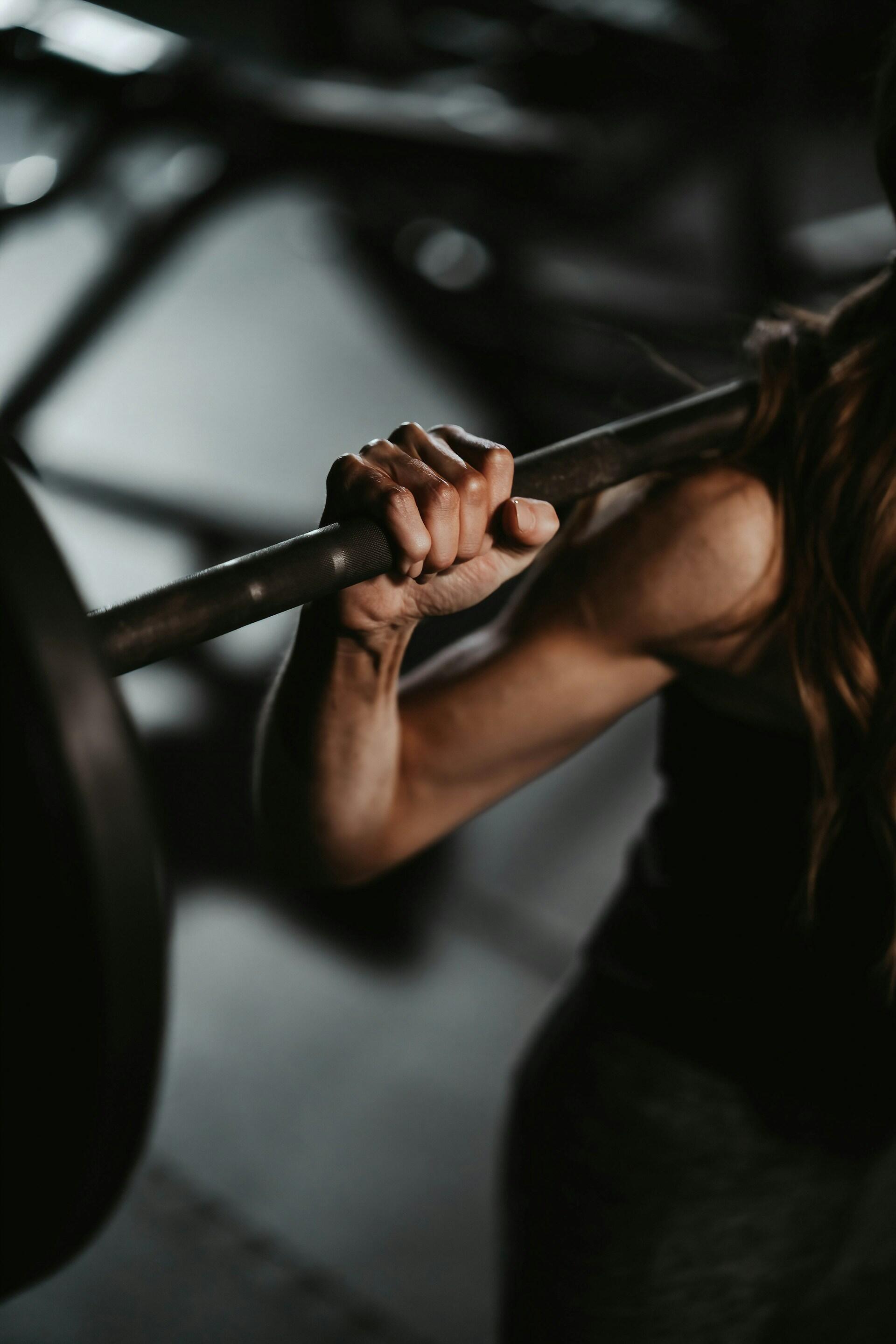 Primer plano de una persona agarrando una barra mientras hace pesas en un gimnasio con poca luz.